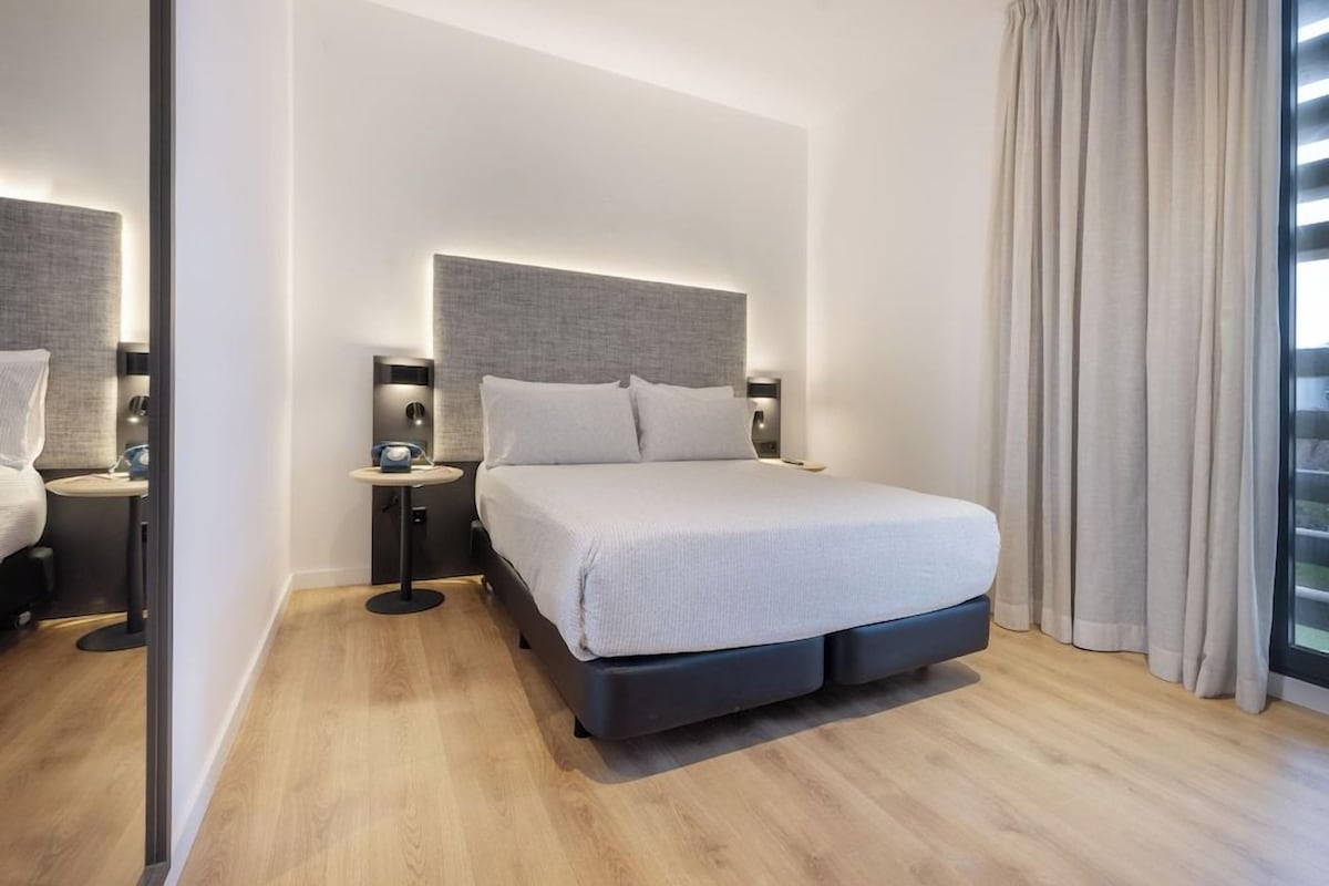 A modern hotel room with a large bed, bedside tables, and a view of the outdoors.