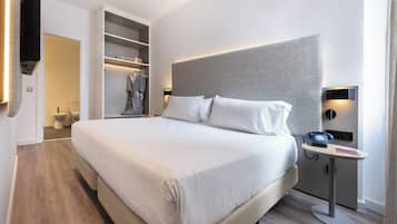 Una habitación de hotel moderna con una cama grande, una mesita de noche con teléfono y un armario empotrado.