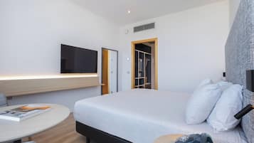 A modern hotel room with a bed, a desk, a chair, a television, and a wardrobe.