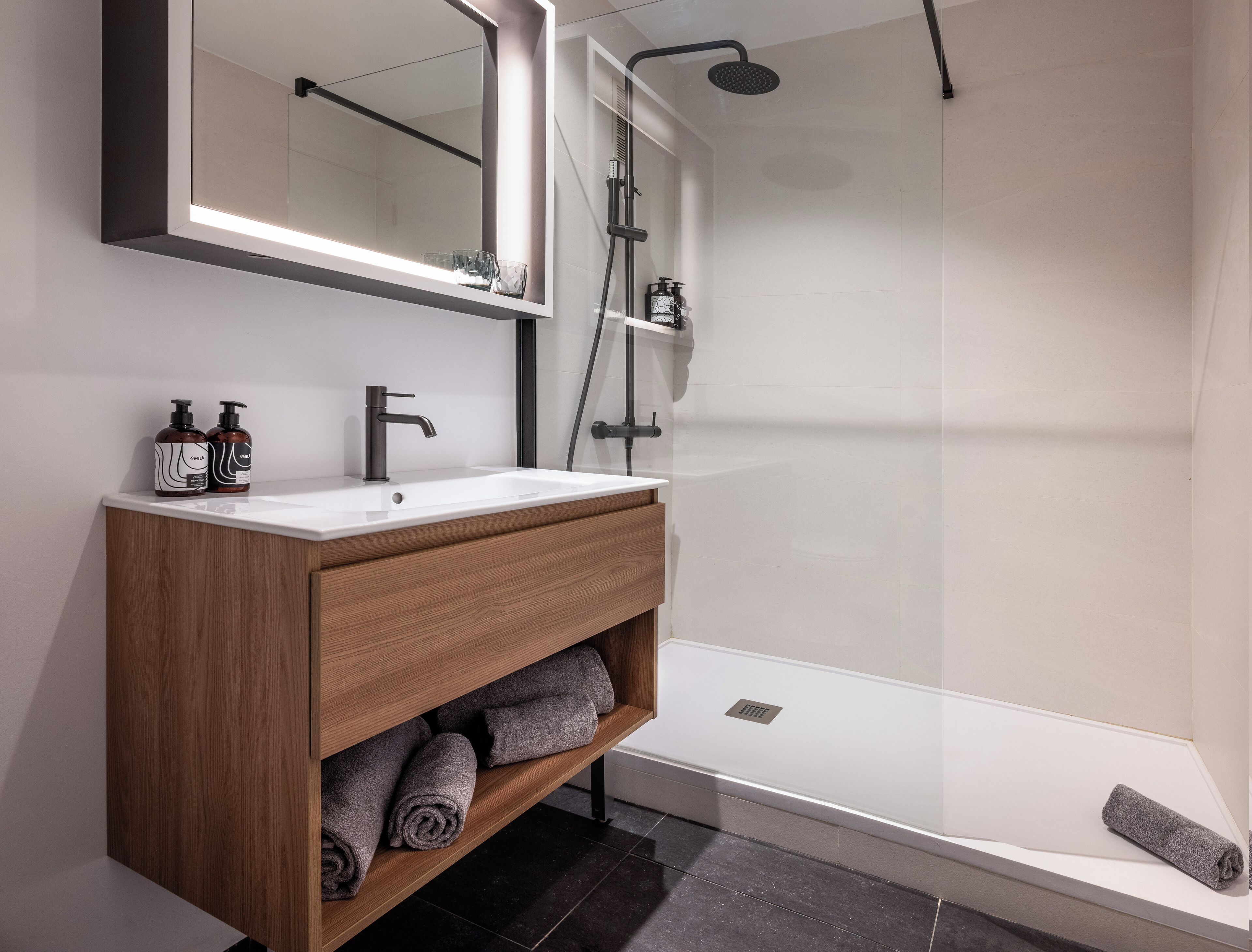 Ein modernes Badezimmer mit Waschtisch aus Holz, einem großen Spiegel und einer Duschkabine.