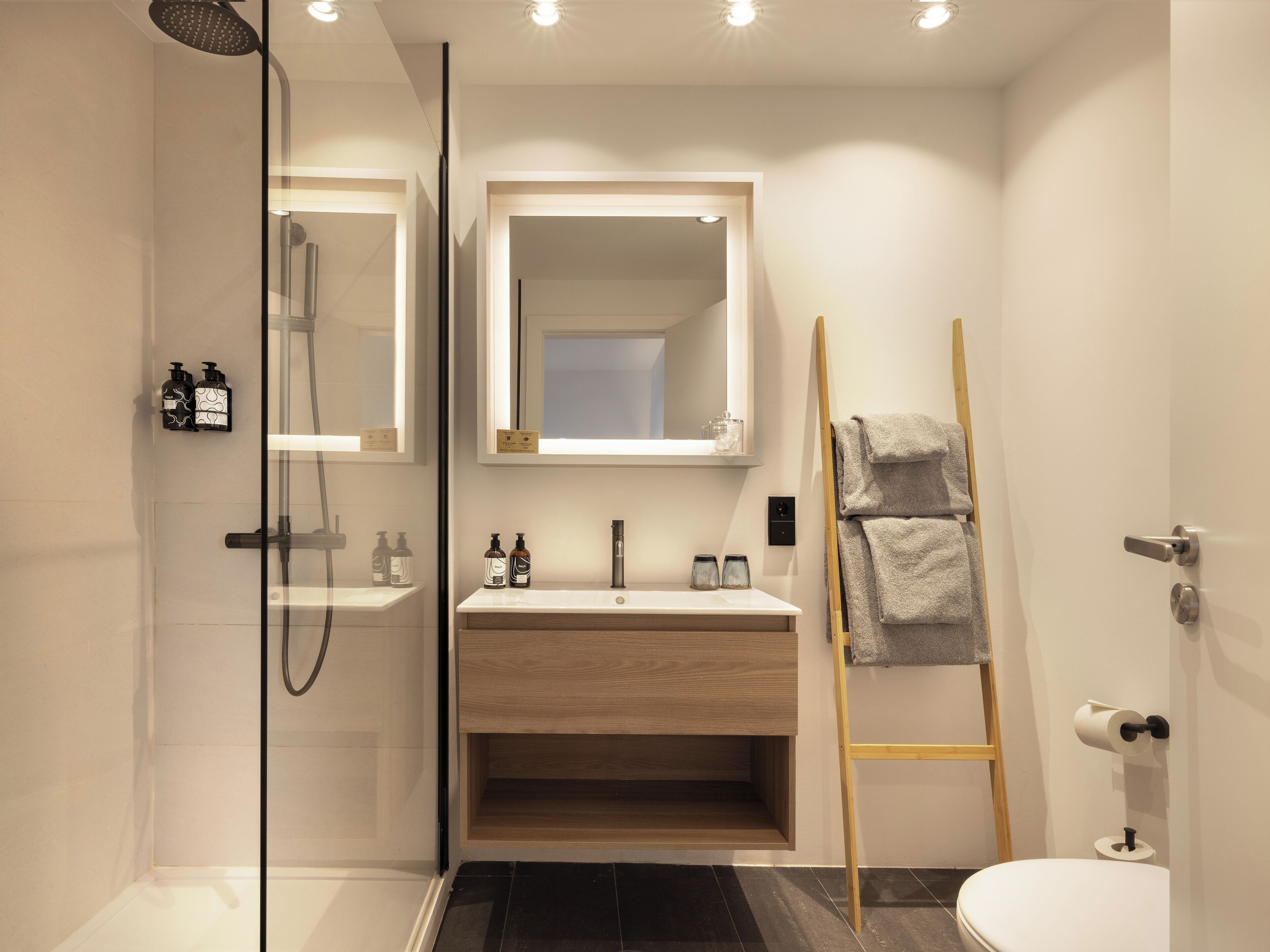 Une salle de bain moderne avec une douche à parois de verre, un meuble-lavabo en bois, un miroir et un porte-serviettes.