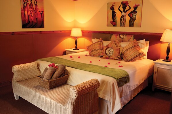 Un dormitorio ordenado con una cama, dos mesitas de noche, un sofá de mimbre y un adorno en la pared.