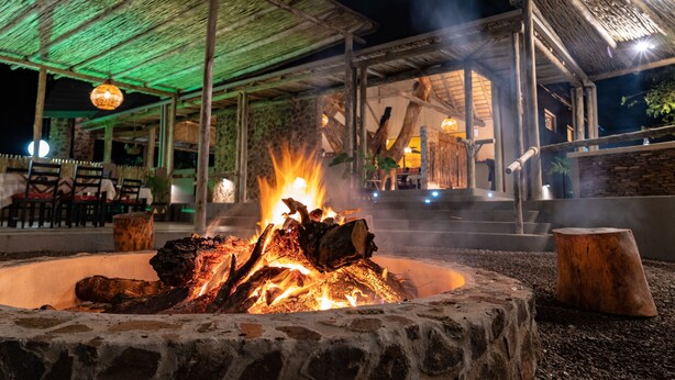 A stone fire pit with logs, surrounded by a stone wall and a wooden bench.