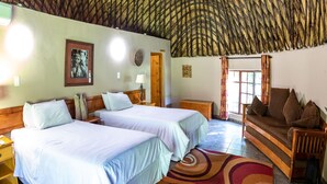 A room with a thatched roof, two beds with white linens, a wooden sofa, and a colorful rug.