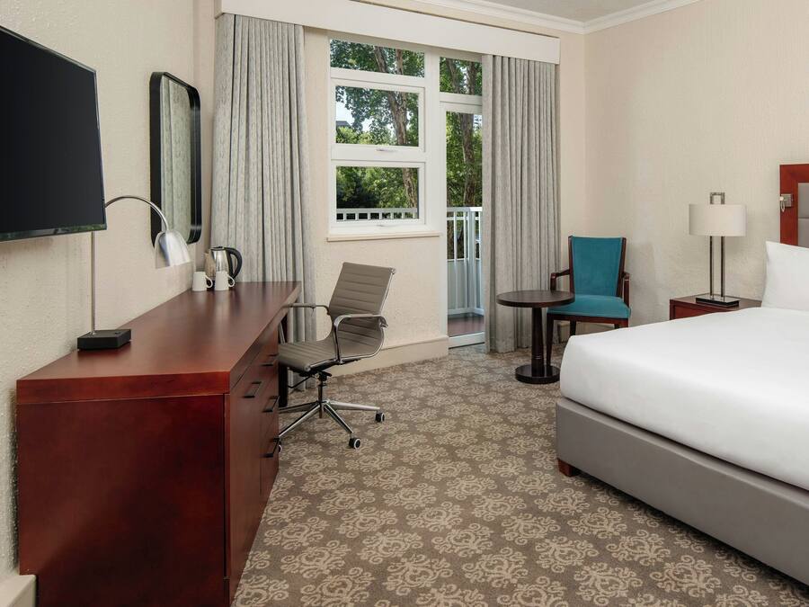 A hotel room with a bed, a desk, a chair, a TV, and a window with curtains.