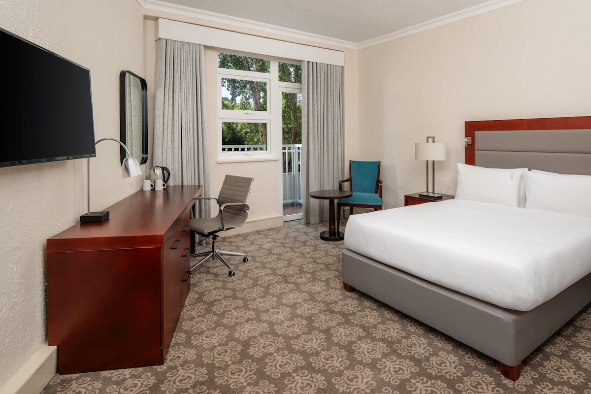 Une chambre d’hôtel avec un grand lit, un bureau avec une chaise, une petite table, un téléviseur et une fenêtre avec des rideaux.
