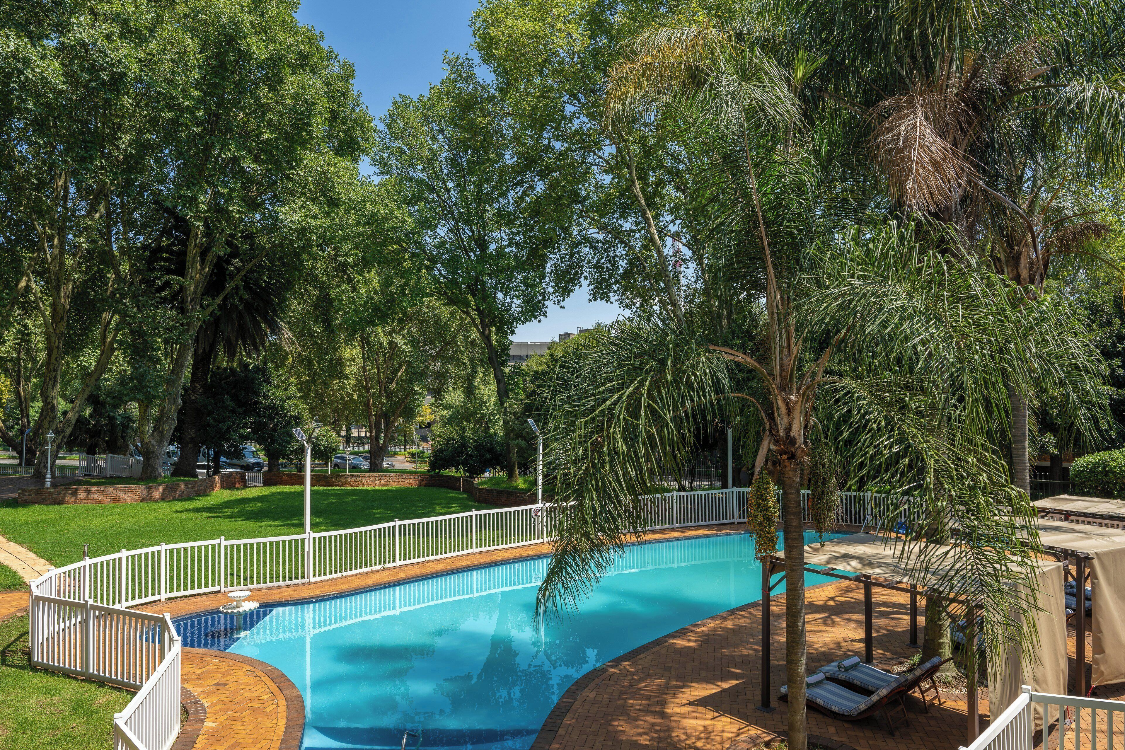Une piscine entourée d’arbres et bordée d’une clôture blanche.