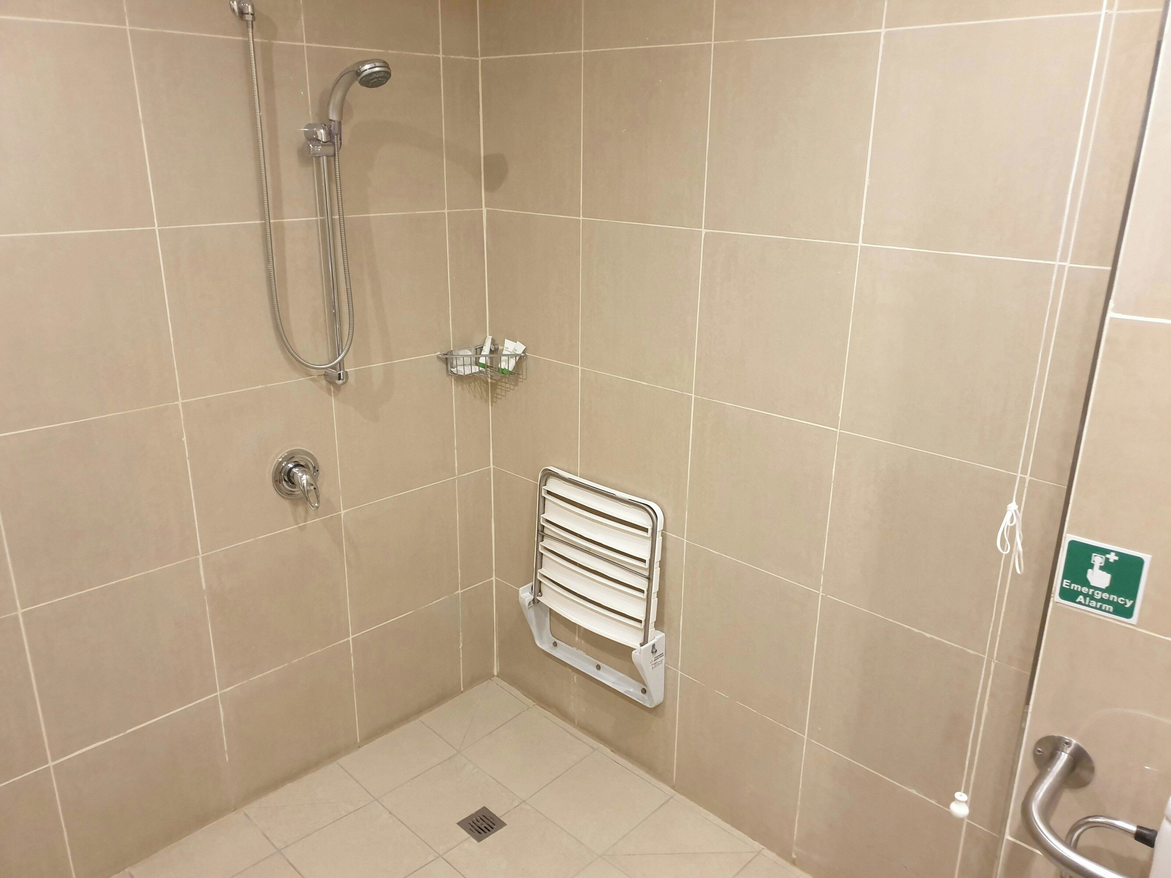 Un espacio de ducha pequeño y cerrado con cabezal de ducha manual, un perchero y una barra de apoyo.