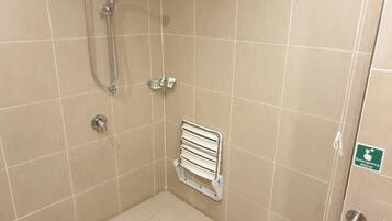 Un espacio de ducha pequeño y cerrado con cabezal de ducha manual, un perchero y una barra de apoyo.