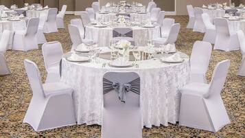 A banquet hall with round tables set for dining, each with white tablecloths and matching chairs.
