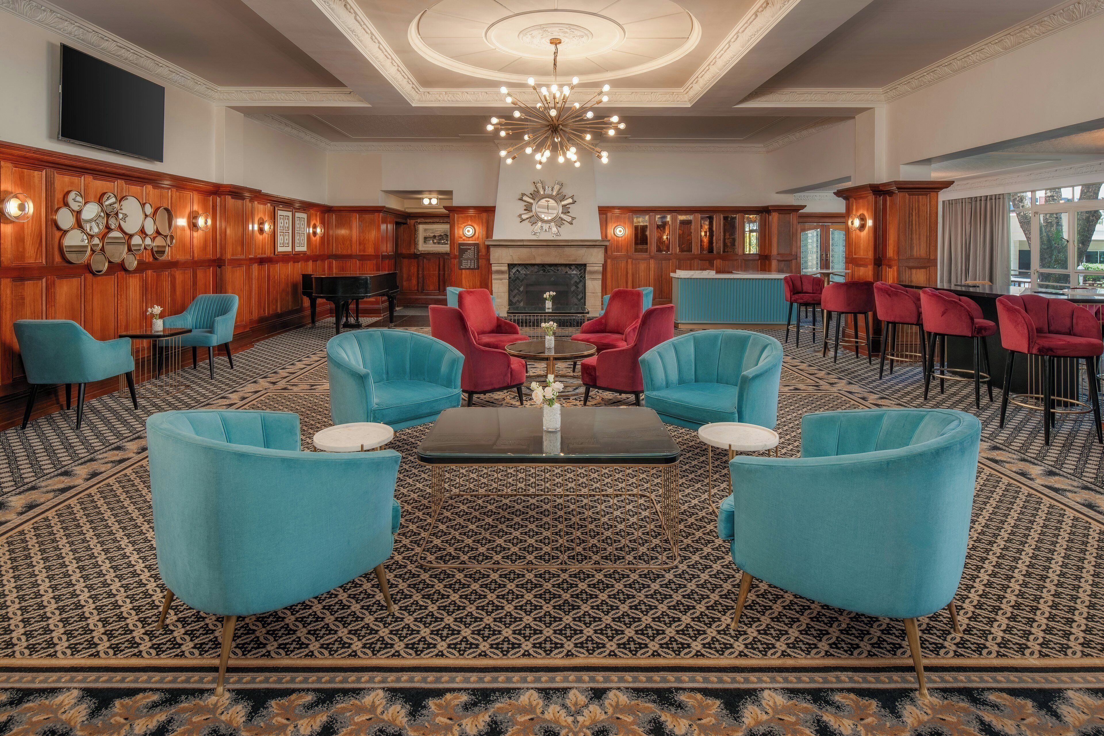 A lobby with a grand chandelier, a piano, and a fireplace. There are multiple seating areas with chairs and a coffee bar.
