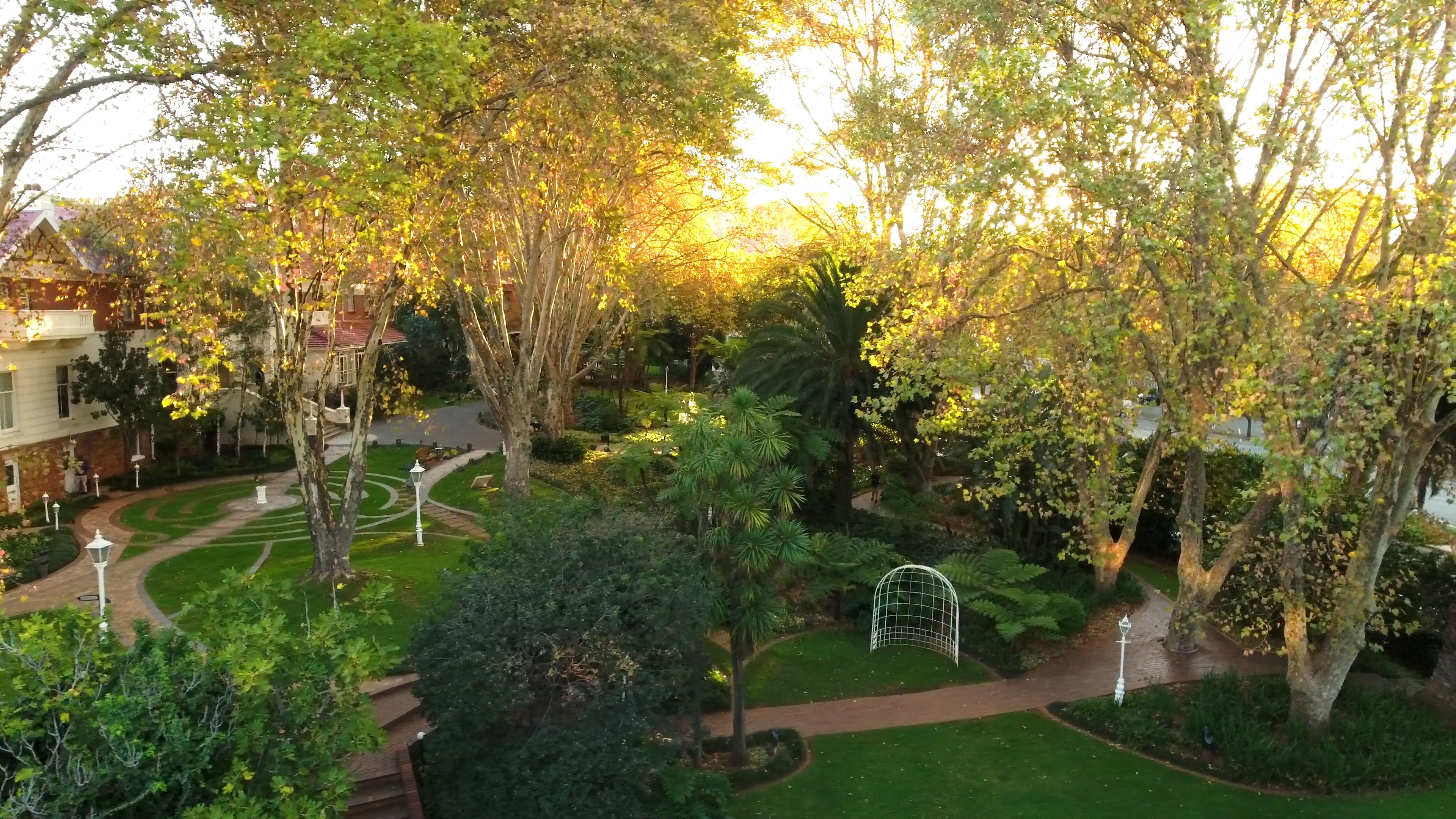 A landscaped garden with pathways, trees, and a white gazebo.