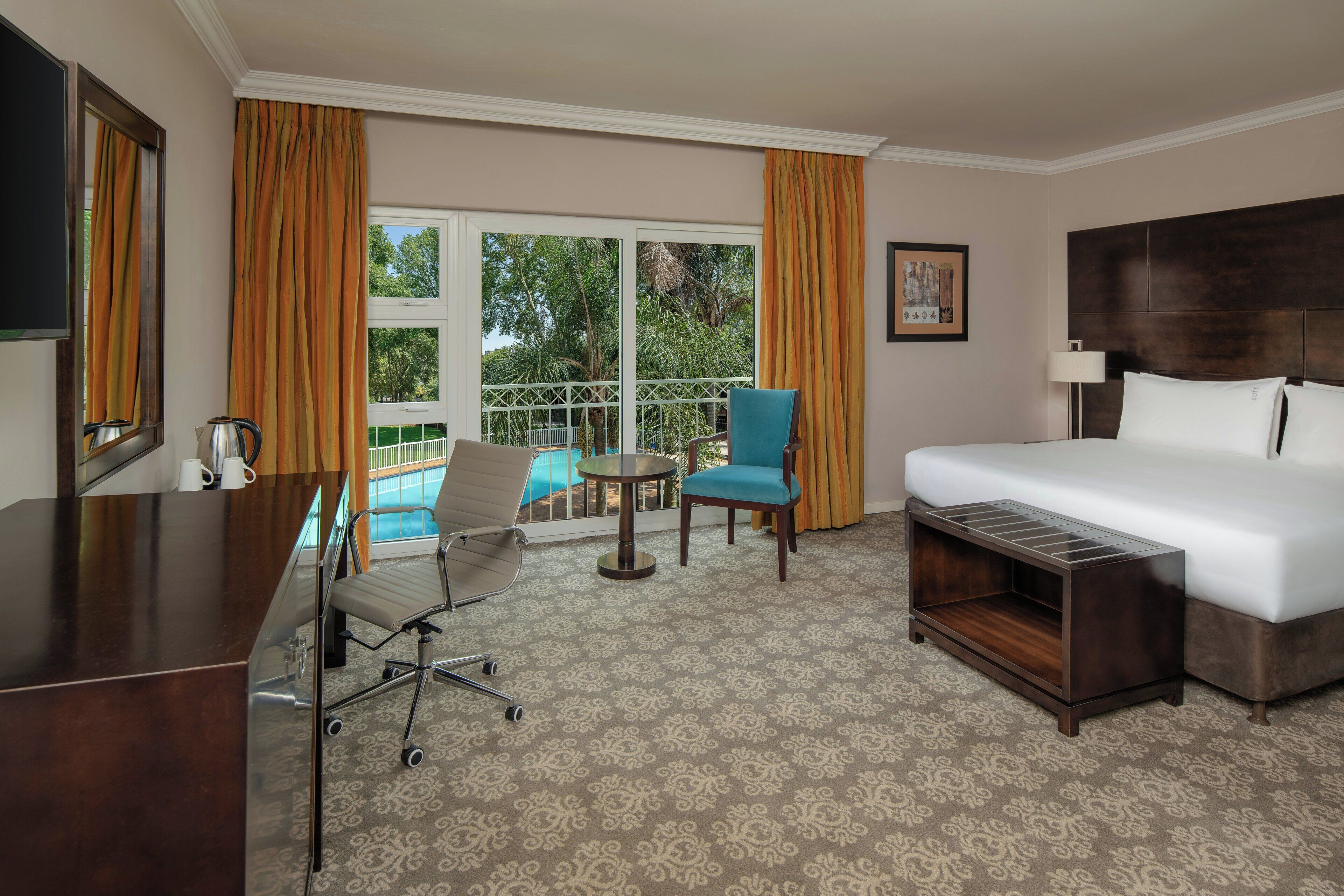 Une chambre d’hôtel avec un lit, un bureau, une chaise, une petite table et une vue sur une piscine.