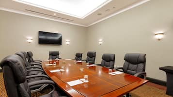 Un salón de conferencias con una larga mesa, varias sillas y un televisor montado.