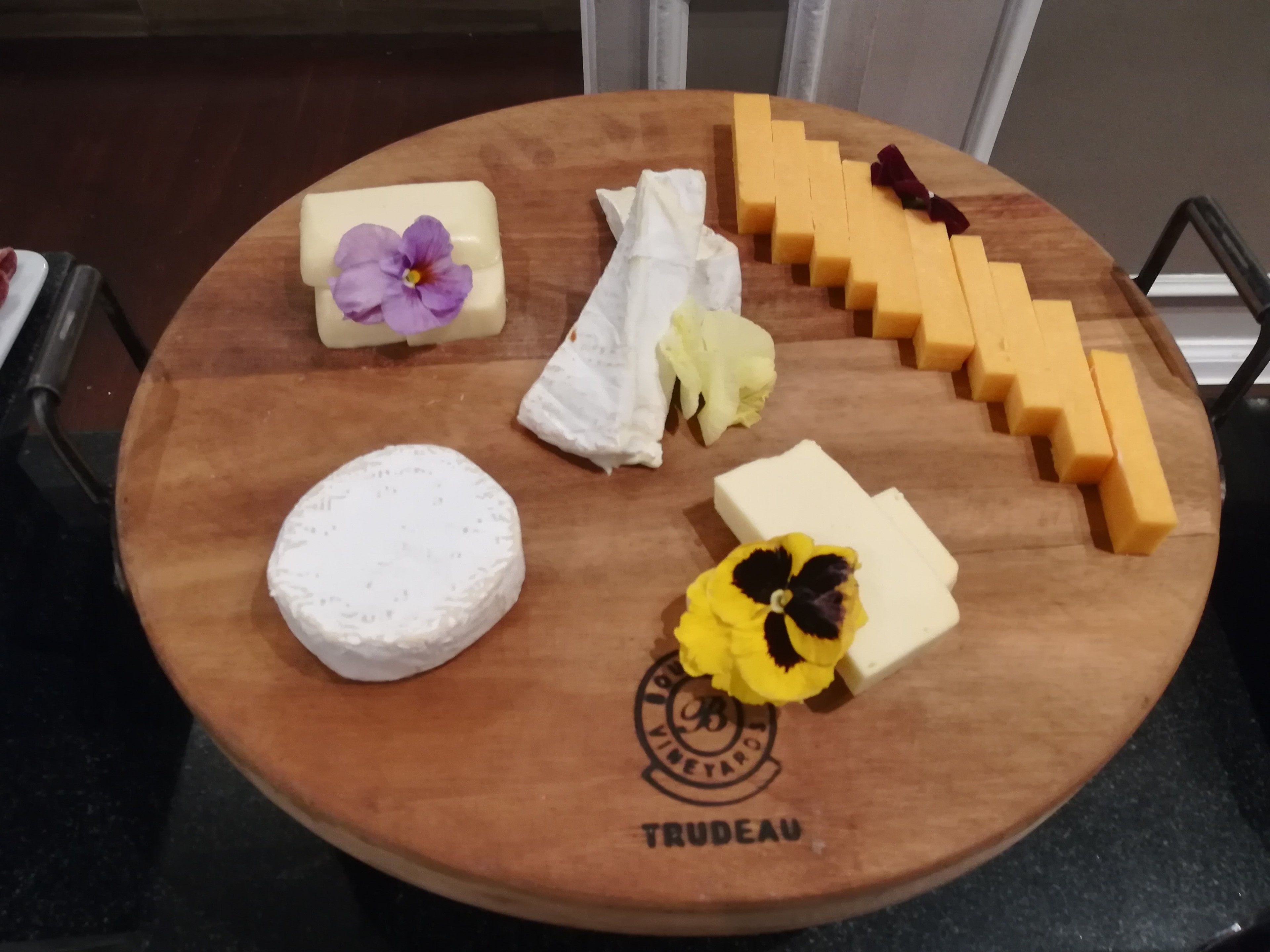 A wooden board with various cheeses and flowers.