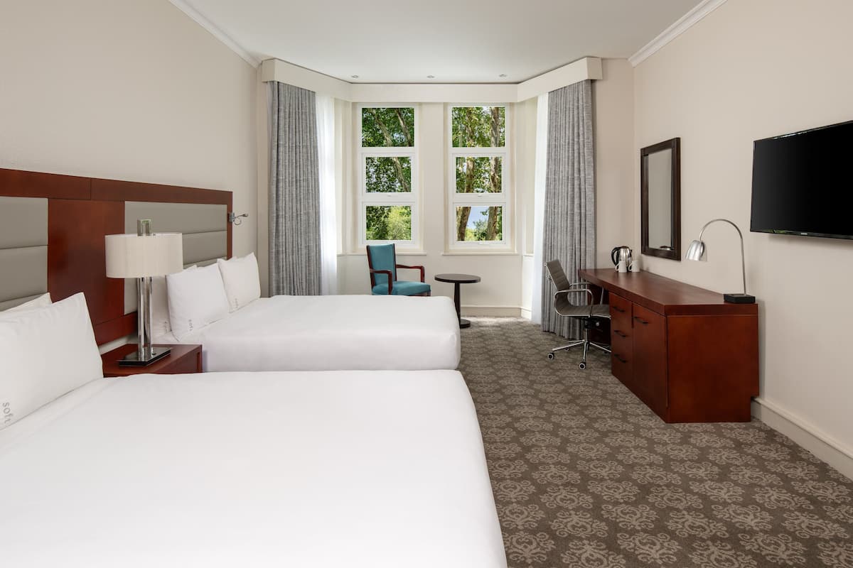 Une chambre d’hôtel avec deux lits, un bureau, une chaise, une télévision et une fenêtre avec des rideaux.