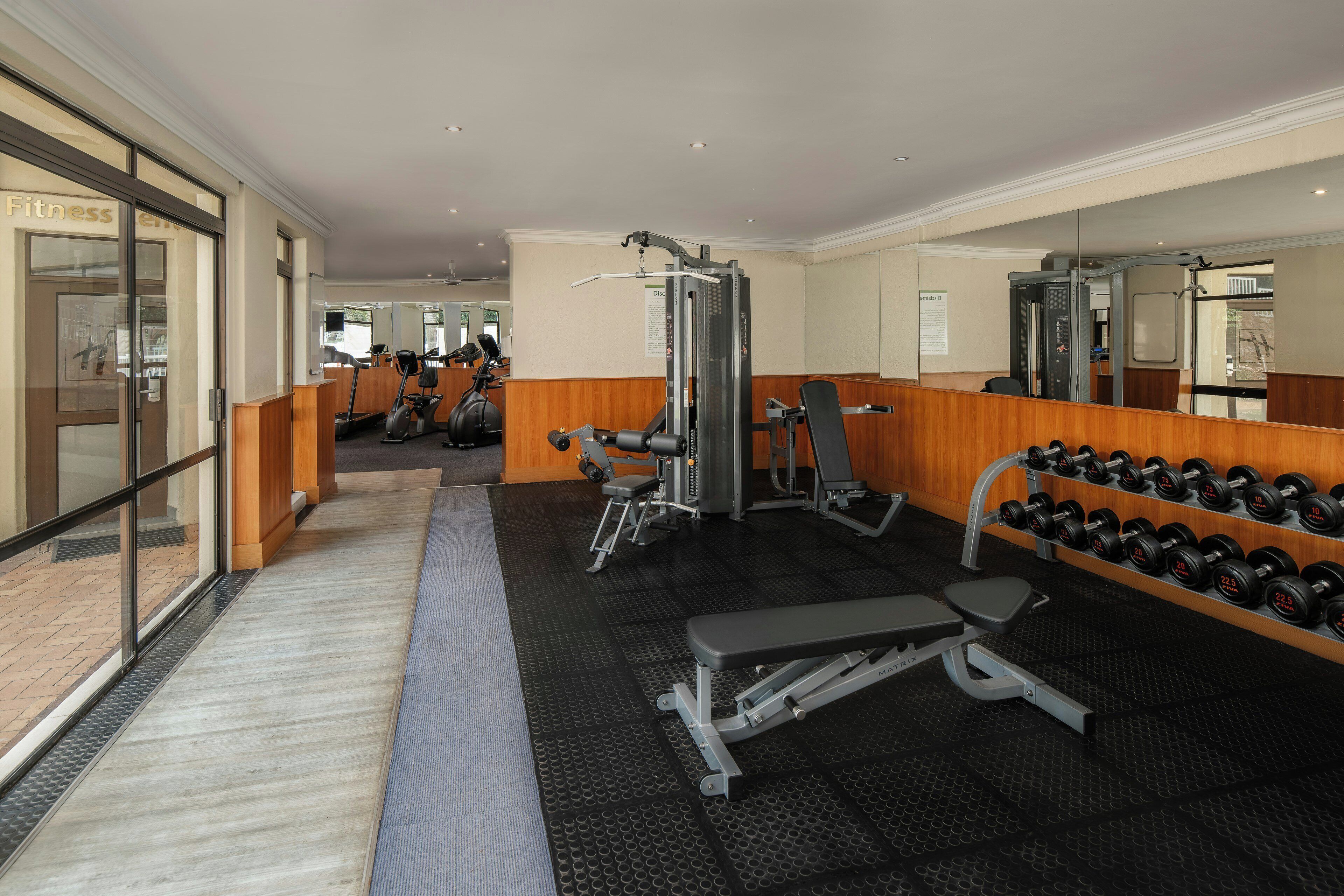 A gym with cardio machines, free weights, and a mirror wall.