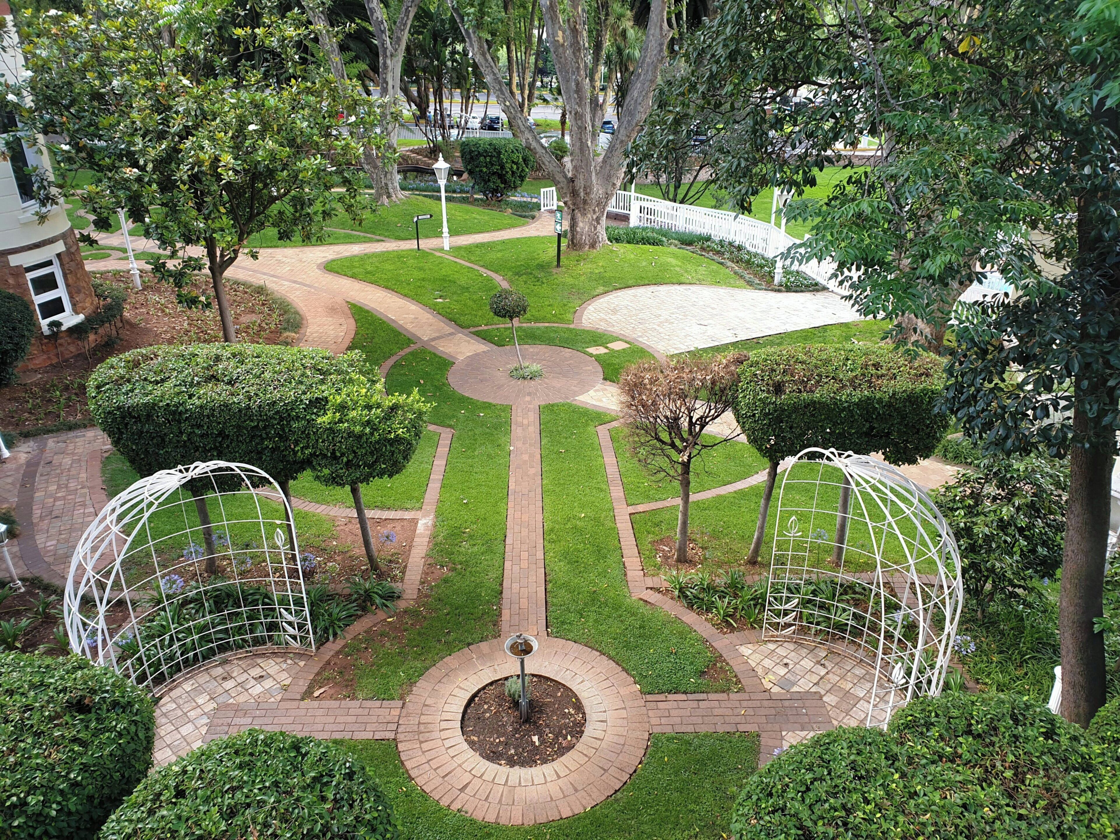 A landscaped garden with a central circular pathway, surrounded by trimmed hedges and trees.