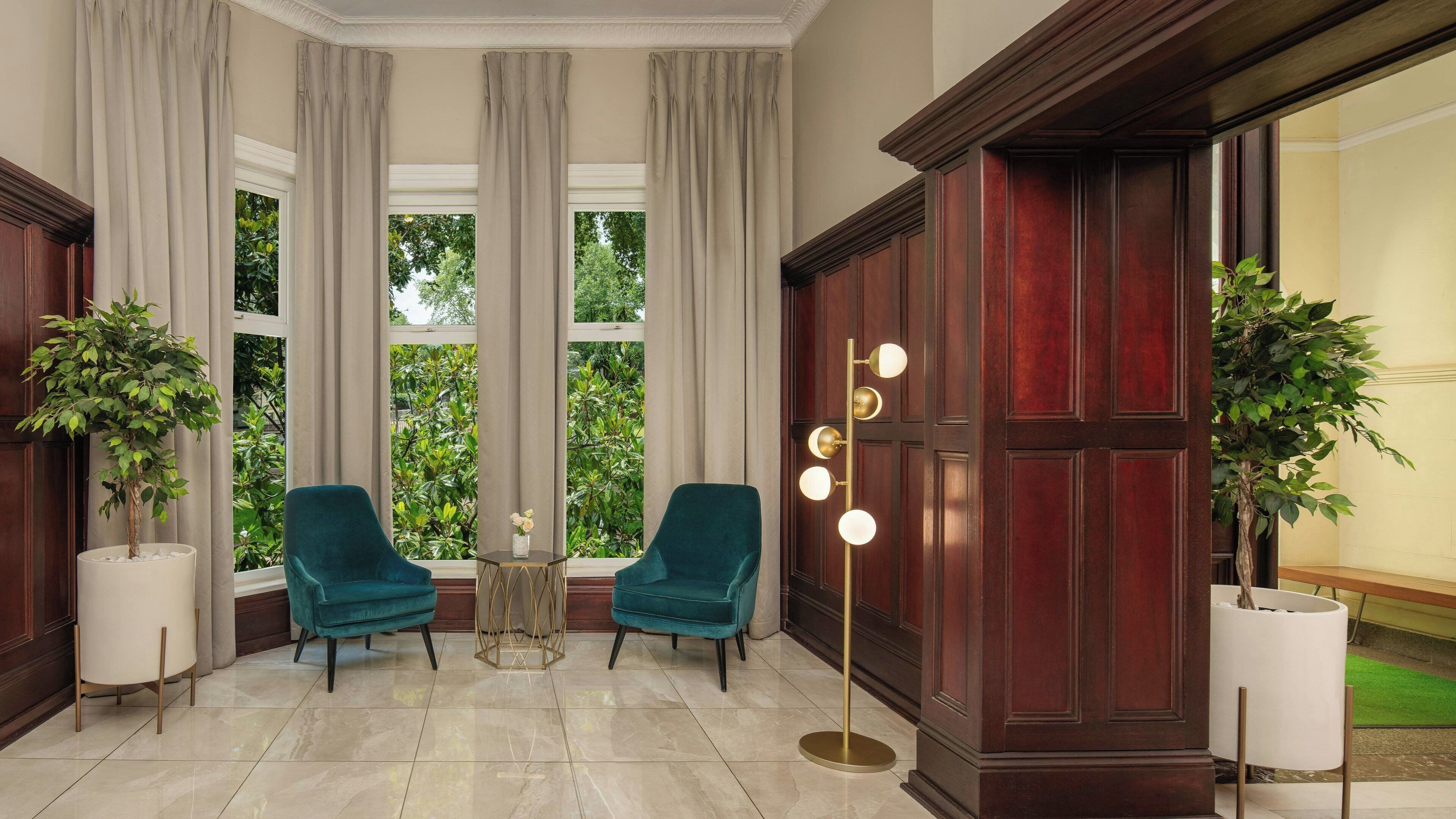 A room with two teal chairs, a floor lamp, and a large window with curtains.