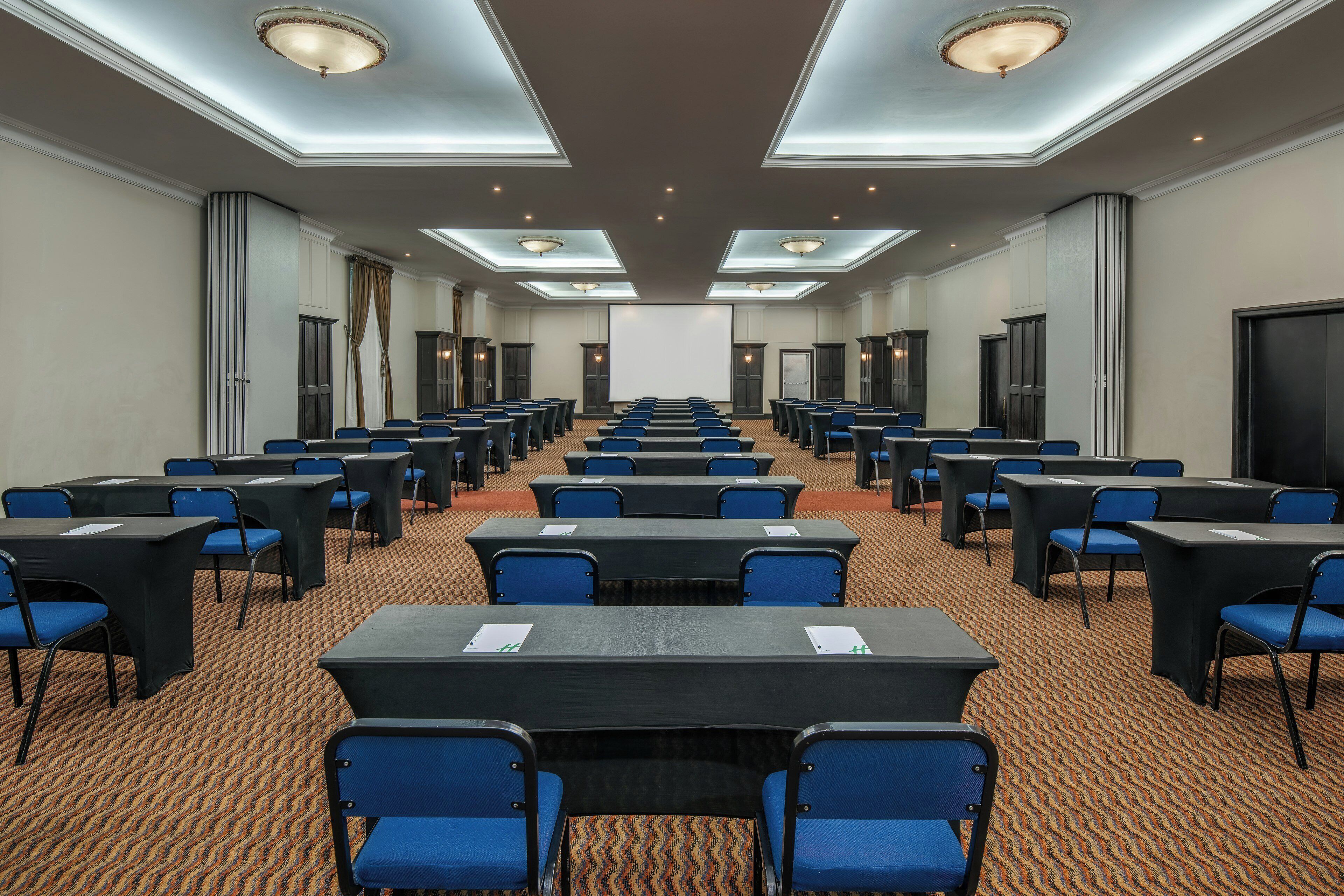 Ein Konferenzraum mit Tischen und Stühlen, einer Projektionsleinwand und einem Teppichboden.