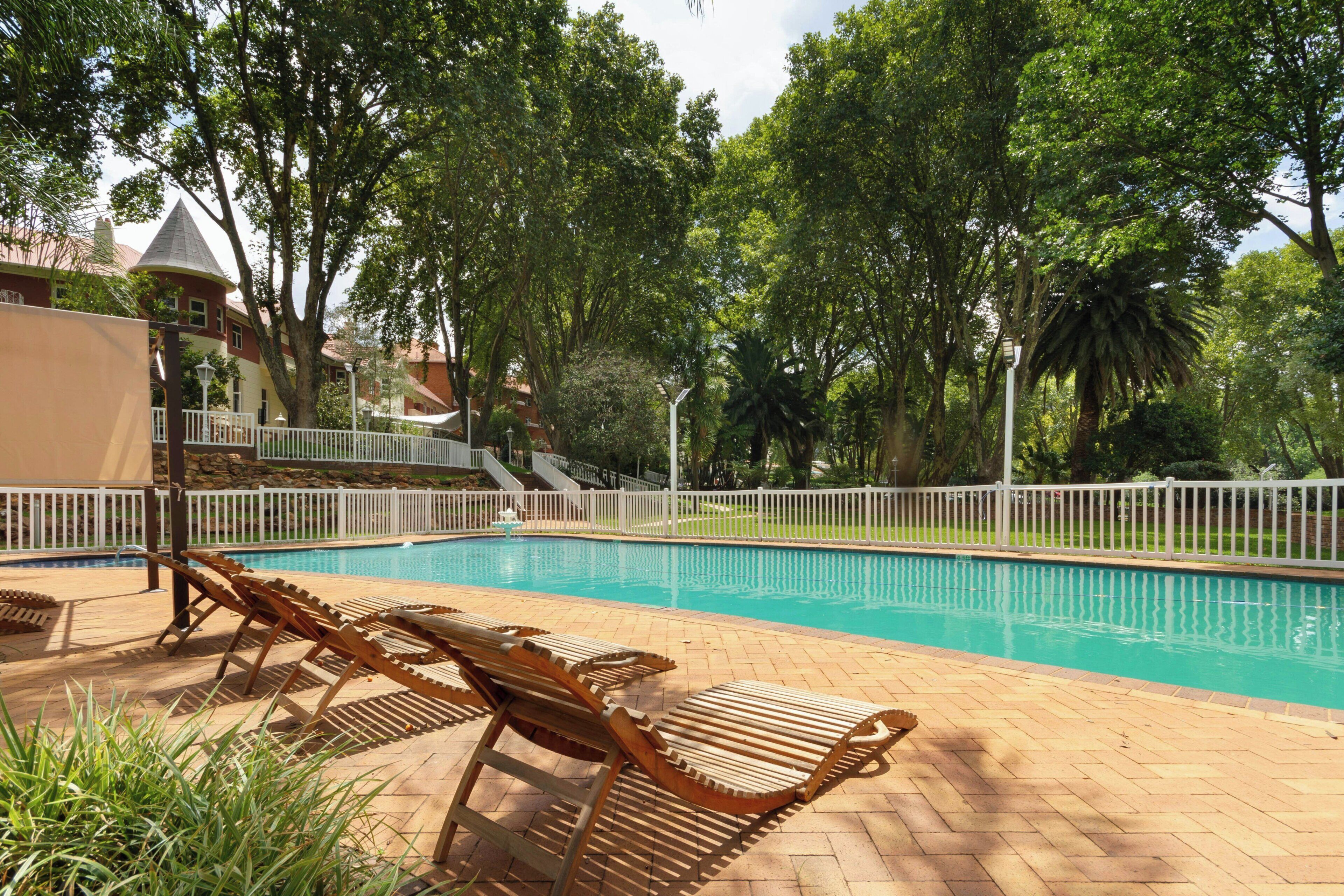 A swimming pool with lounge chairs and a white fence.