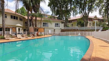 A swimming pool with lounge chairs, surrounded by a white fence and trees.
