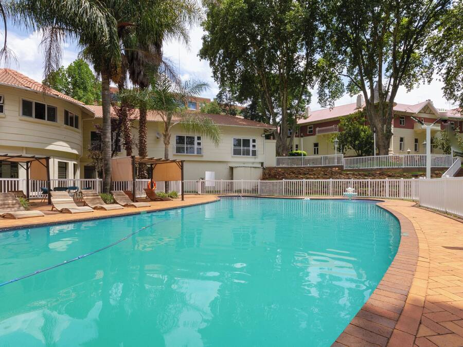 A swimming pool with lounge chairs, surrounded by a white fence and trees.