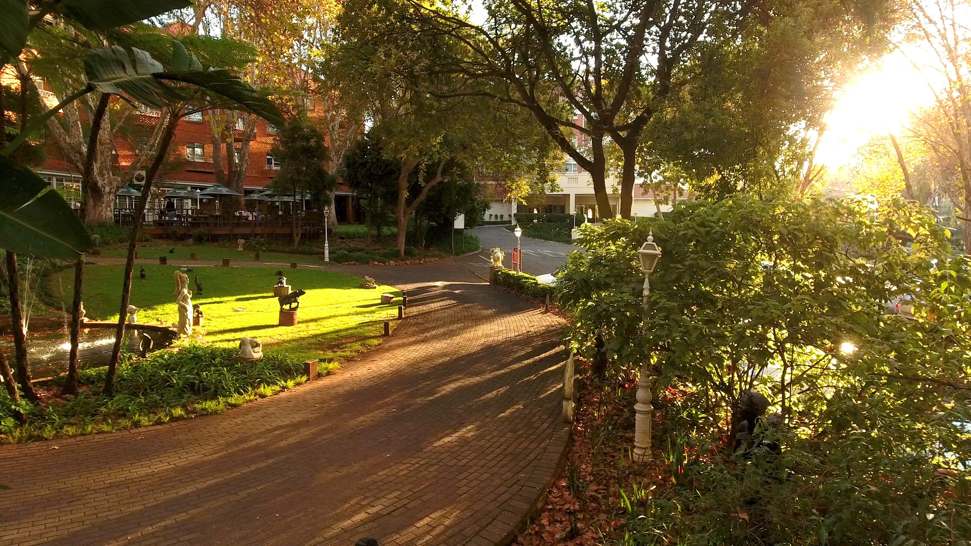 A paved pathway in a park with statues and benches.
