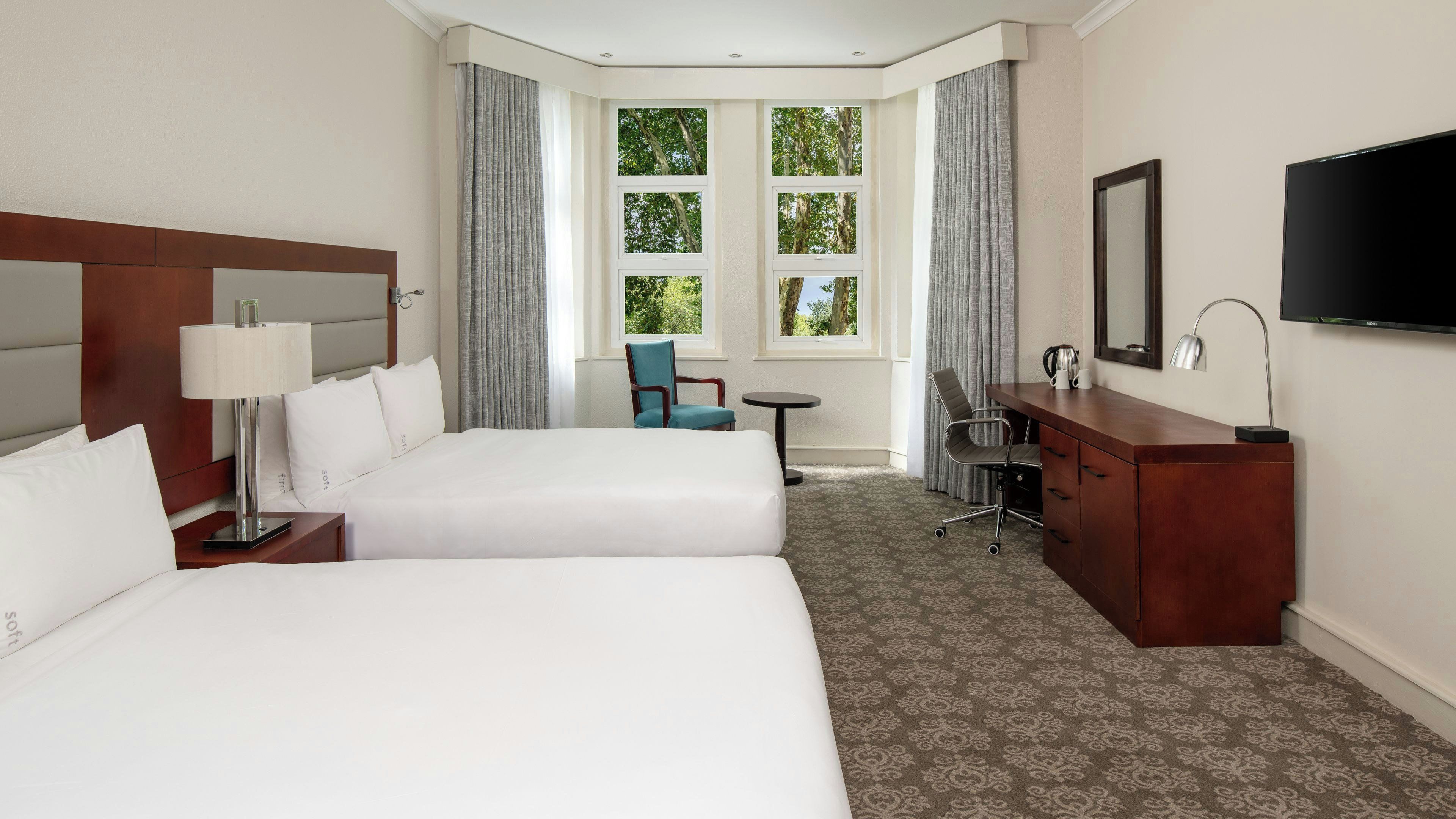 A hotel room with two beds, a desk, a chair, a TV, and a window with curtains.