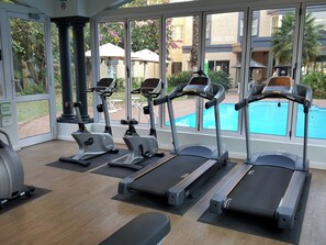A fitness center with treadmills, stationary bikes, and a pool visible through large windows.