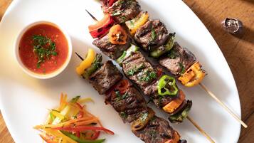 Brochettes de viande et de légumes grillés, servies sur une assiette blanche, accompagnées d’une sauce salsa et d’un quartier de citron vert.