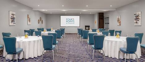 Una sala conferenze con tavoli rotondi, sedie color acquamarina e un grande schermo che mostra "FOUR POINTS BY SHERATON".