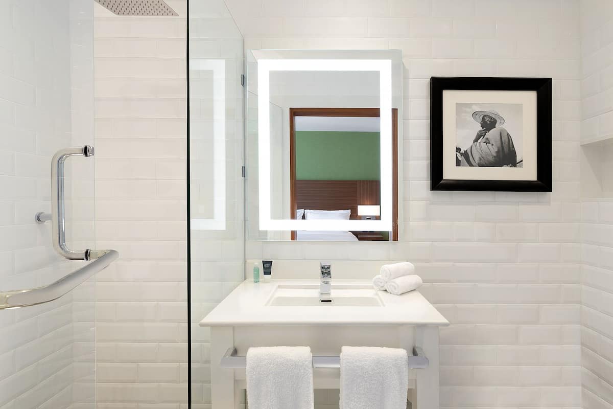 Uma casa de banho moderna com cabine de duche em vidro, lavatório branco e fotografia a preto e branco emoldurada na parede.