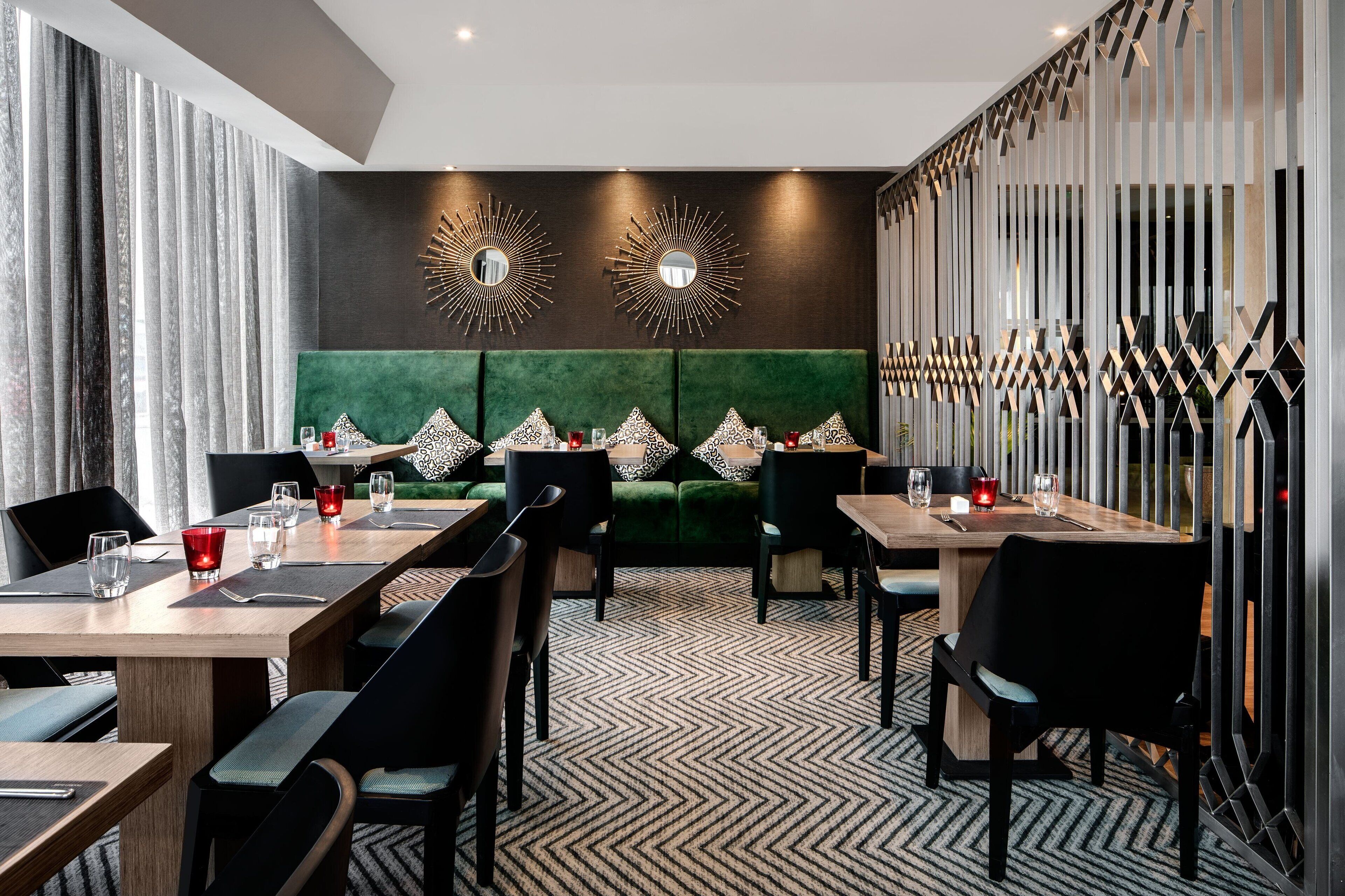 A modern dining area with a green upholstered sofa, black chairs, and a patterned floor.