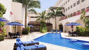 A swimming pool with lounge chairs and umbrellas, surrounded by palm trees and potted plants. - Four Points by Sheraton Dar es Salaam New Africa (Dar es Salaam)