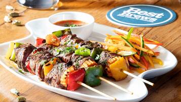 A plate of skewered meat and vegetables, a tall glass of beer, and a coaster with "Best Brews" text.