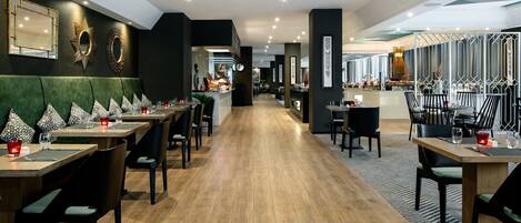 A modern restaurant with a long wooden floor, green upholstered booths, and black chairs.