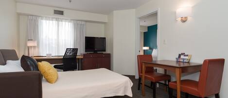 A hotel room with a bed, a desk with a chair, a television, and a window with curtains.