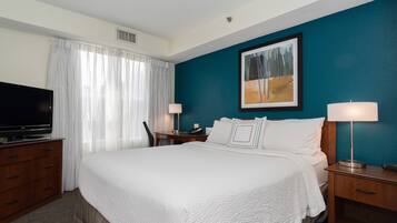 A hotel room with a large bed, a TV, a desk with a lamp, and a painting on the wall.