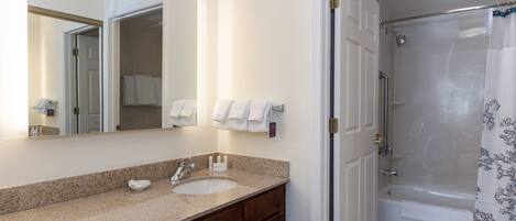 A bathroom with a sink, mirror, and shower area.