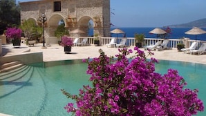 A pool area with lounge chairs and umbrellas, a stone building with arches, and a view of the sea. - Patara Prince Hotel & Resort (Kas)