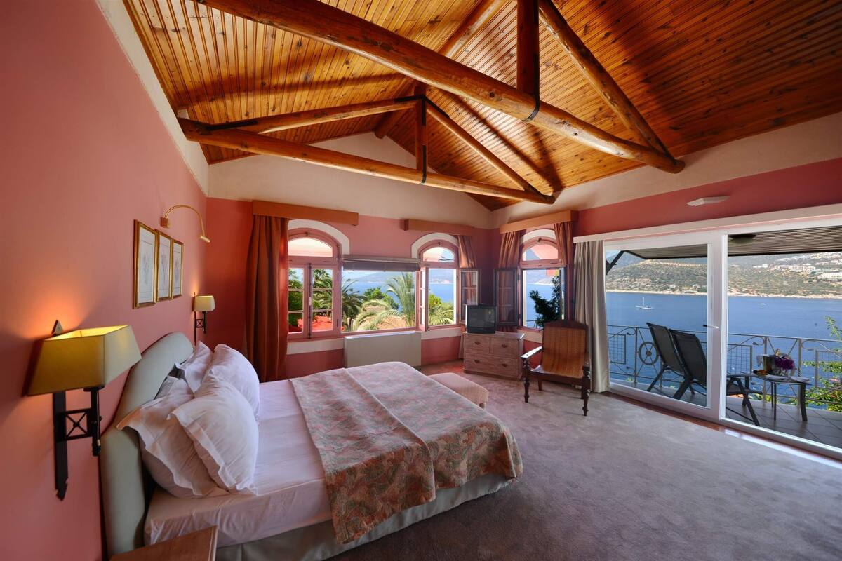 A bedroom with a bed, a desk, and a view of the sea.