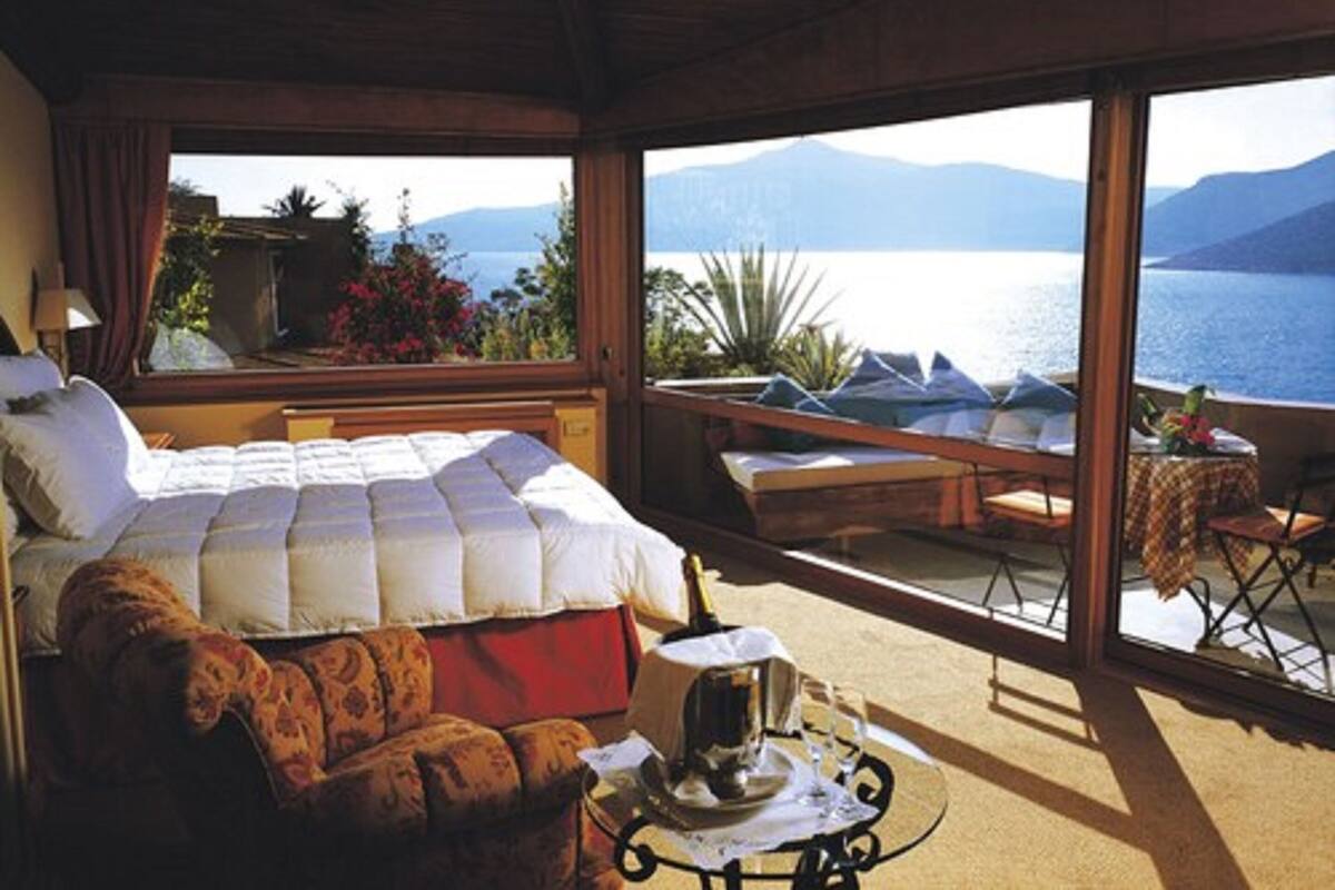 A bedroom with a large bed, a sofa, and a balcony with a view of the sea and mountains.