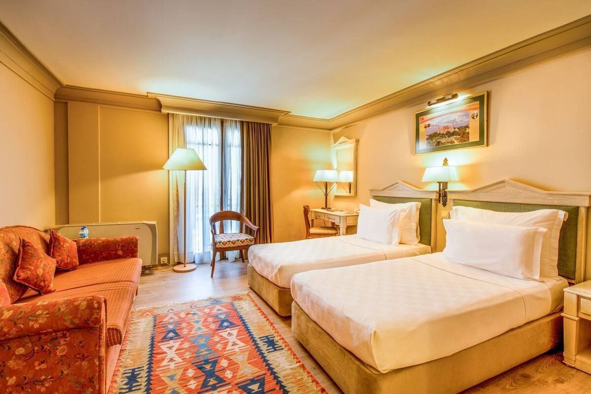 A hotel room with two beds, a sofa, a desk, and a chair.