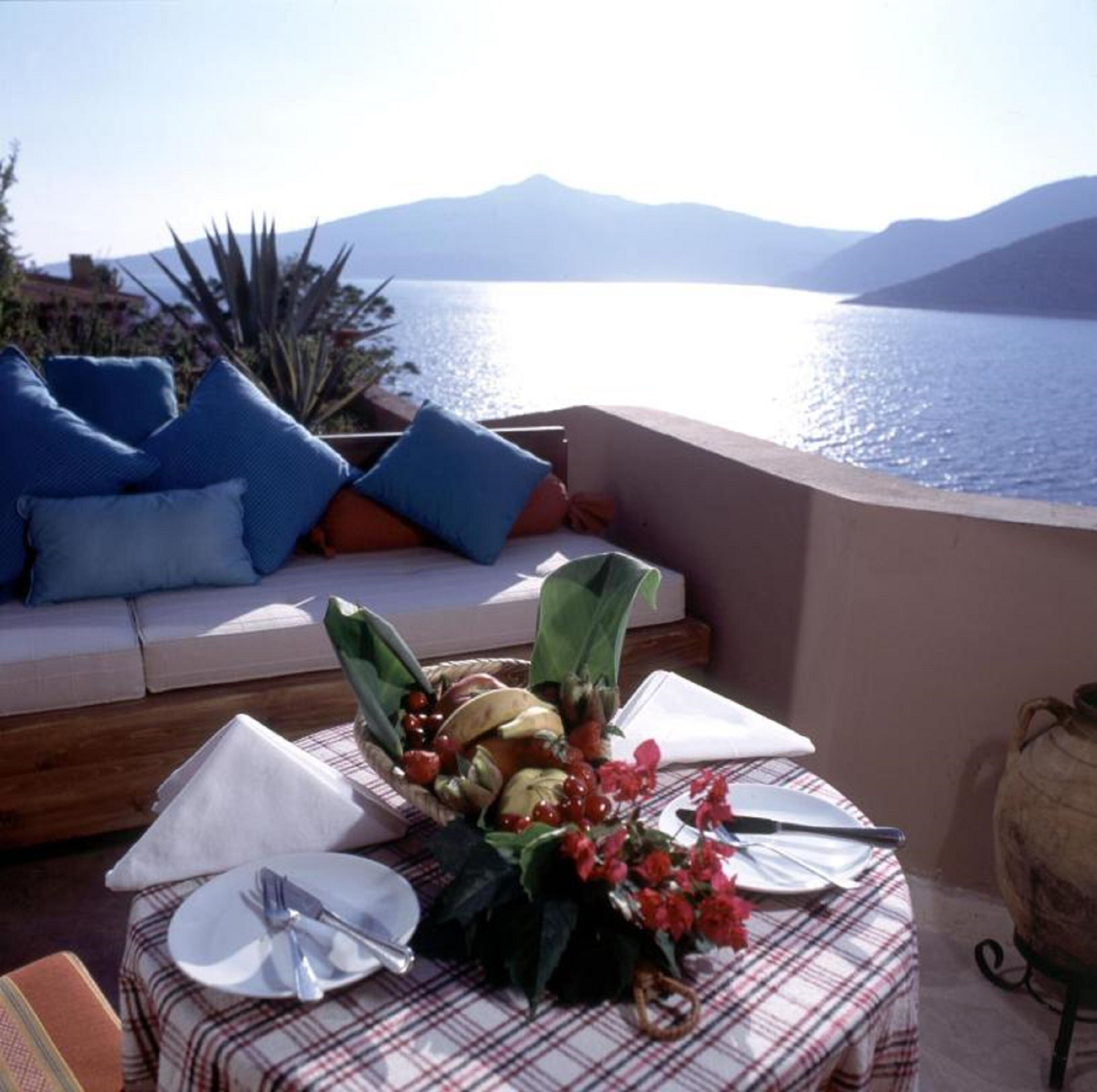 Una terraza con sofá, mesa de comedor y vistas al mar y a las montañas.