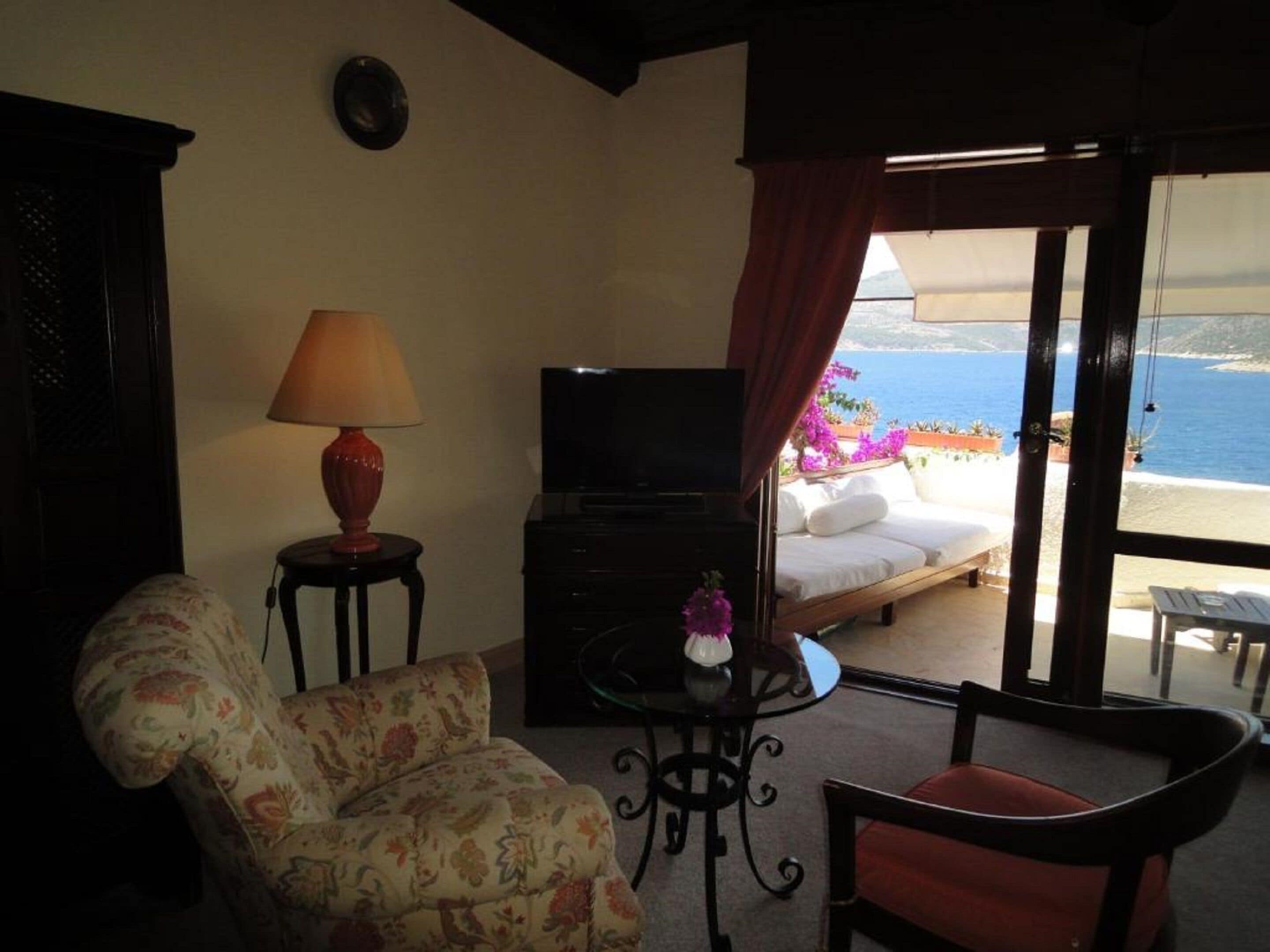 Una habitación con sofá, televisor, una mesita con lámpara y cama con vista al mar.