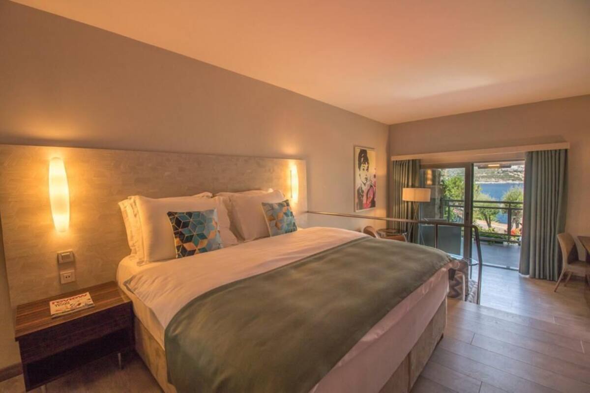 A hotel room with a large bed, a nightstand, a desk, and a view of the outdoors.