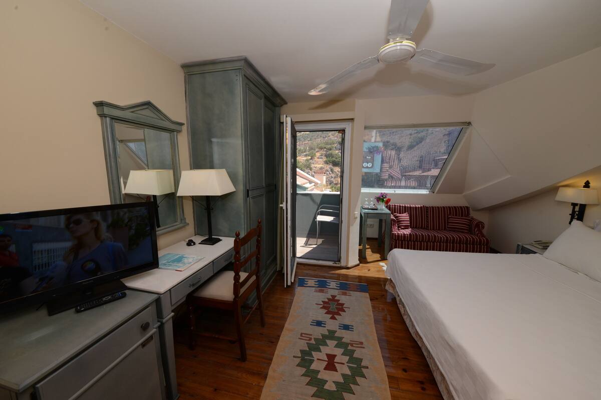 A hotel room with a TV, desk, chair, bed, and a view of the outdoors.