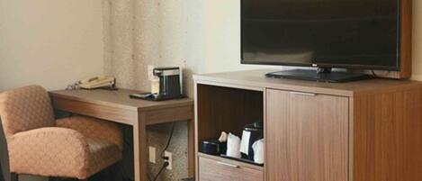 A hotel room with a wooden desk, a television, a chair, and a cabinet with drawers.