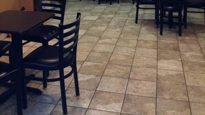 Ein Restaurantinneres mit Fliesenboden, Holztischen und -stühlen, einem Hinweisschild für den Notausgang und einer Klimaanlage an der Wand.